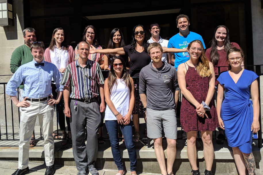 Image of members of the lab outside the lab building on Meyran Ave. Dr. Luna is in the center with her arms spread to the camera.